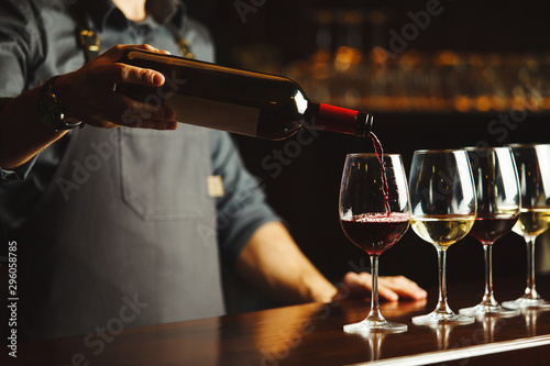 Bartender pours red wine in glasses on wooden bar counter