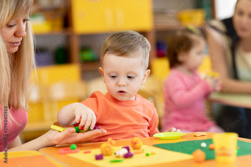 Fototapeta premium Little kid boy learning to use colorful play clay in kindergarten. Babies group studying in creche or nursery