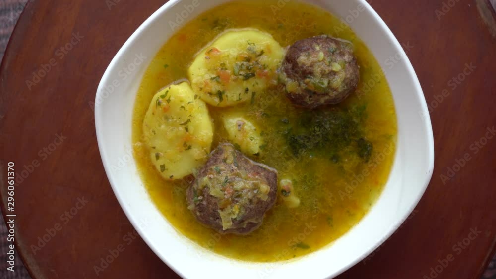 Sopa de albóndigas y papa hervida rotando sobre plataforma de madera en una mesa