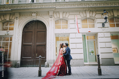 Beautiful woman in a long red dress walks around the city with her husband in a blue suit and with a beard © prostooleh