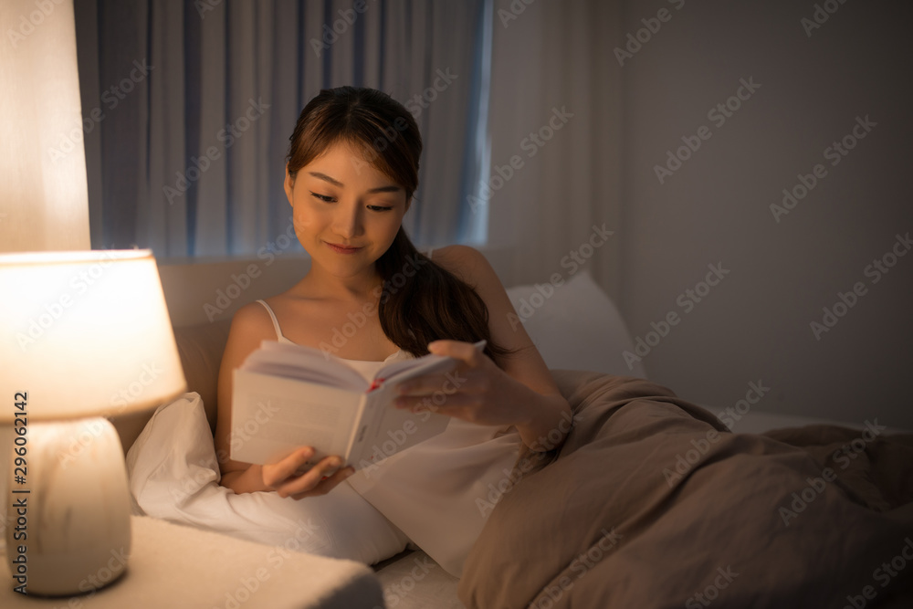 leisure and people concept - young woman reading book in bed at night home leisure and people concept - young woman reading book in bed at night home