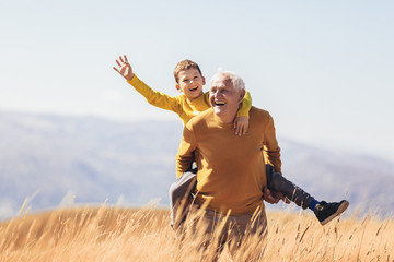 Grandson piggyback with his grandfather in autumn.