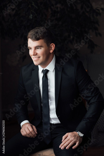 Stylish groom. The groom is dressed at home in a suit. Cute groom posing for a photographer. Groom getting ready in the room for wed day.