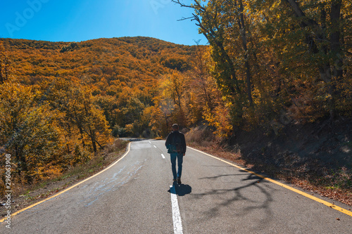 Traveler on road among yellow autumn mountain forest