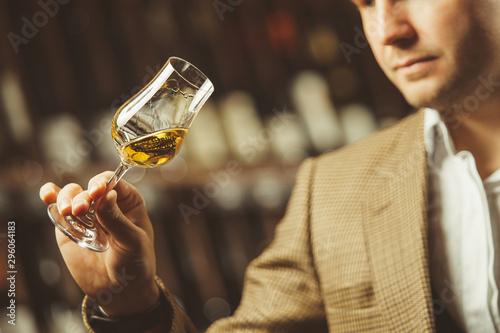 Bokal of whiskey on background, male sommelier appreciating drink photo