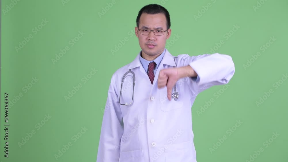 Angry Asian man doctor with eyeglasses giving thumbs down Angry Asian man doctor with eyeglasses giving thumbs down