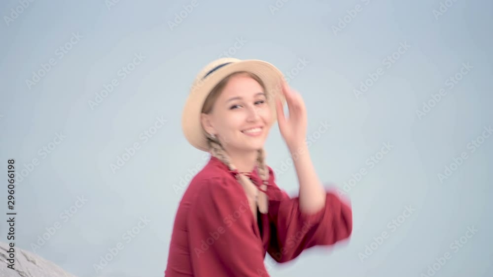 Portrait attractive caucasian young woman in a red dress and a straw hat with pigtails turns around sitting on the seashore smiling looking at the camera Portrait attractive caucasian young woman in a red dress and a straw hat with pigtails turns around sitting on the seashore smiling looking at the camera