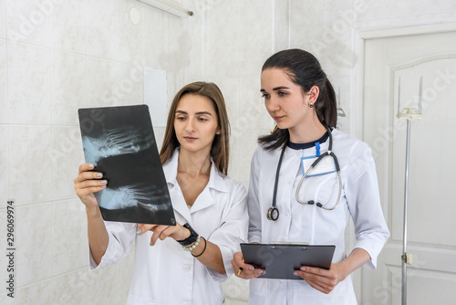 Two young doctors discussing patient's foot x-ray. One doctor holding film opposite herself and other holding clipboard
