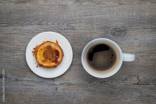 Traditional Portuguese Pastel de Nata tart with a cup of black coffee on a wooden table