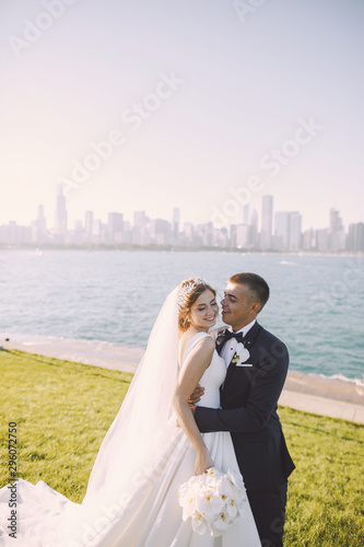 Elegant bride in a white dress and veil. Handsome groom in a blue suit. Couple in a summer park near river photo