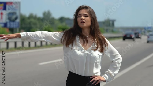 beautiful young brunette woman trying to stop passing by cars on the road