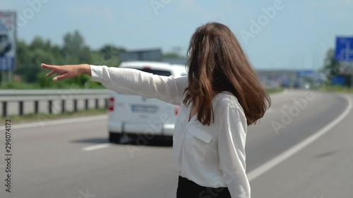 beautiful young brunette woman trying to stop passing by cars on the road looks desperate