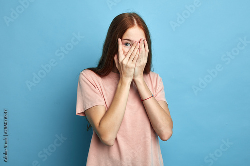 Stressed scared girl covering her face with palm, feeling afraid of stressful situstion,beautiful stylish girl hiding her face behind palms.close up portrait. isolated blue background photo