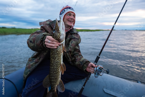Young amateur happy angler holds the Pike fish (Esox lucius) in his hand being on the lake.