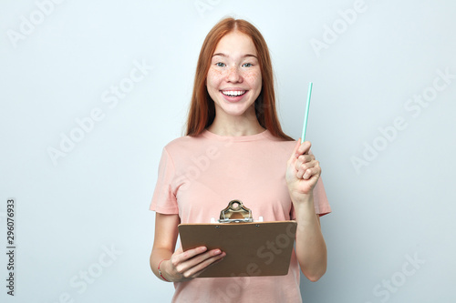 Obraz na plátně cheerful ginger woman holding a pen and clipboard