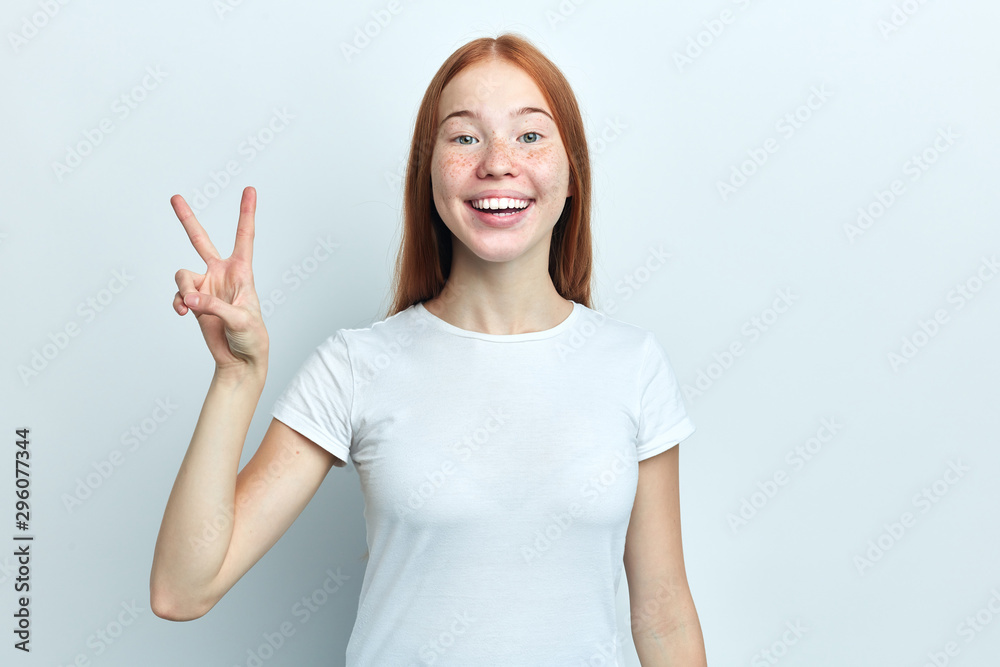 Attractive positive girl with freckles is showing peace sign and smiling. . Isolated on white background and copy space. close up portrait, body language Attractive positive girl with freckles is showing peace sign and smiling. . Isolated on white background and copy space. close up portrait, body language