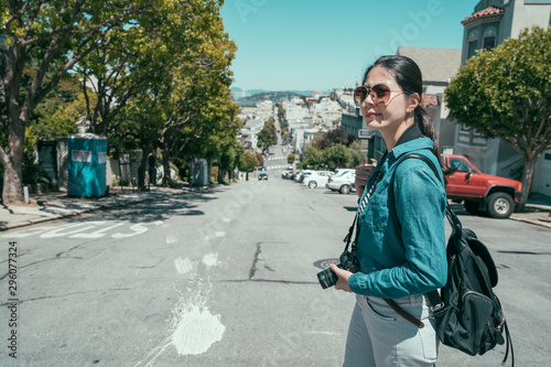Young female photographer taking photograph on vintage camera outdoors on lombard street. tourist girl with backpack enjoying summer trip in san francisco sightseeing in russian hill on sunny flare