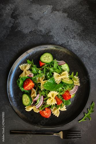 italian pasta salad farfalle, vegetables, mix leaves (tomato, cucumber, onion, lettuce, chard, arugula and more) menu concept. food background. copy space. Top view