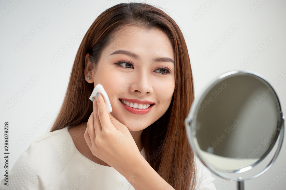 Taking off her make-up. Beautiful cheerful young woman using cotton disk and looking at her reflection in mirror with smile while sitting at the dressing table Taking off her make-up. Beautiful cheerful young woman using cotton disk and looking at her reflection in mirror with smile while sitting at the dressing table
