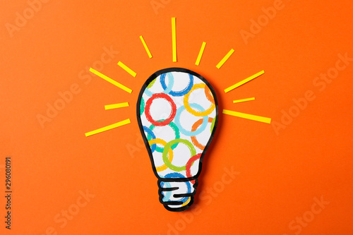 Light bulb with multicolored circles on orange background, space for text