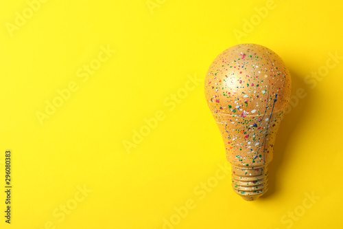 Light bulb with paint splatters on yellow background, space for text