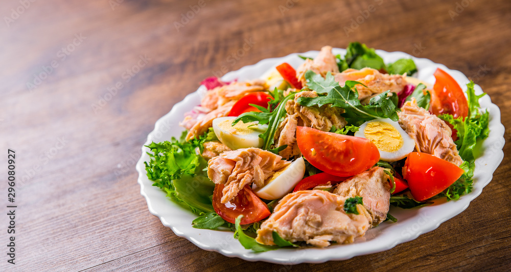 Fresh salad with fish, arugula, eggs,red pepper, lettuce, fresh sald leaves and tomato on a white plate on wooden table background Fresh salad with fish, arugula, eggs,red pepper, lettuce, fresh sald leaves and tomato on a white plate on wooden table background