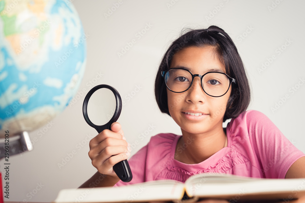 Asian girl wearing glasses is smiling and using a magnifying glass in the classroom, Educational concept Asian girl wearing glasses is smiling and using a magnifying glass in the classroom, Educational concept