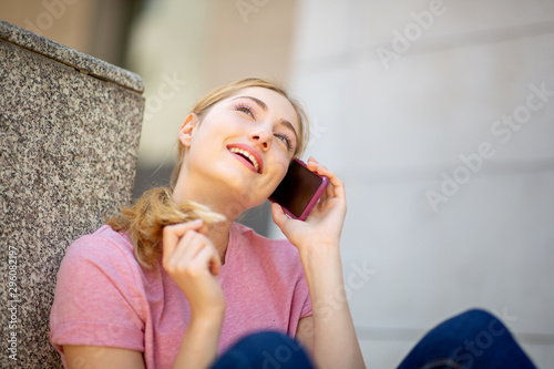 smiling teen girl sitting outside and talking with mobile phone