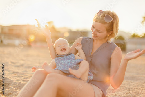 Young happy mother with her little daughter having fun while sitting on the beach on sunset © Demetrio