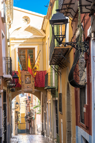 Villajoyosa, Comunitat Valenciana / Spain - July 29th, 2019: Acrh in a narrow street with the Spanish and local flags in the town center photo