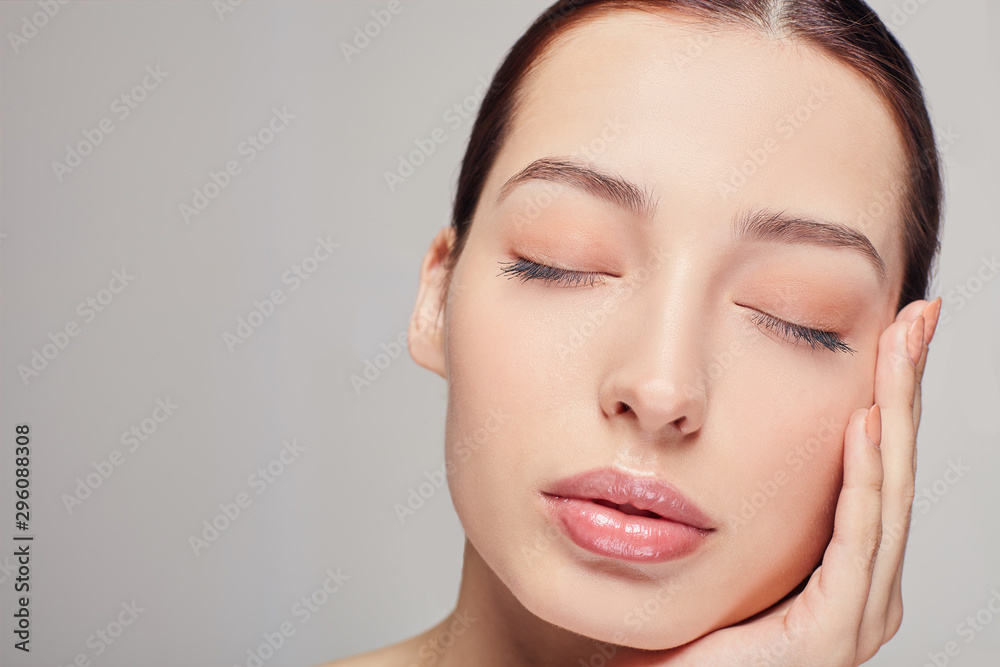 An excellent sophisticated girl with dark hair and radiant clean delicate skin on the gray background. Lady put her head on her hand. Looks straight. Cosmetology, face skin care. An excellent sophisticated girl with dark hair and radiant clean delicate skin on the gray background. Lady put her head on her hand. Looks straight. Cosmetology, face skin care.