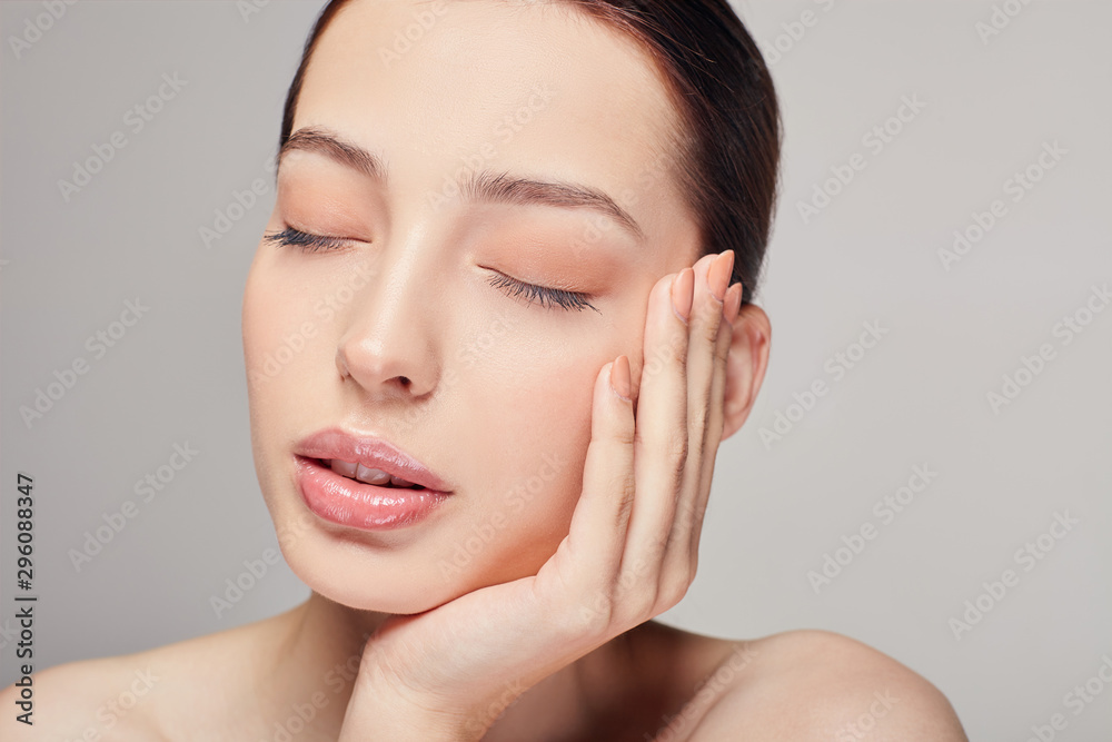 An elegant sophisticated beautiful girl, brown hair and clean delicate skin on the gray background. Lady put her head on her hand. Close eyes. Spa, face skin care. Wellness. An elegant sophisticated beautiful girl, brown hair and clean delicate skin on the gray background. Lady put her head on her hand. Close eyes. Spa, face skin care. Wellness.