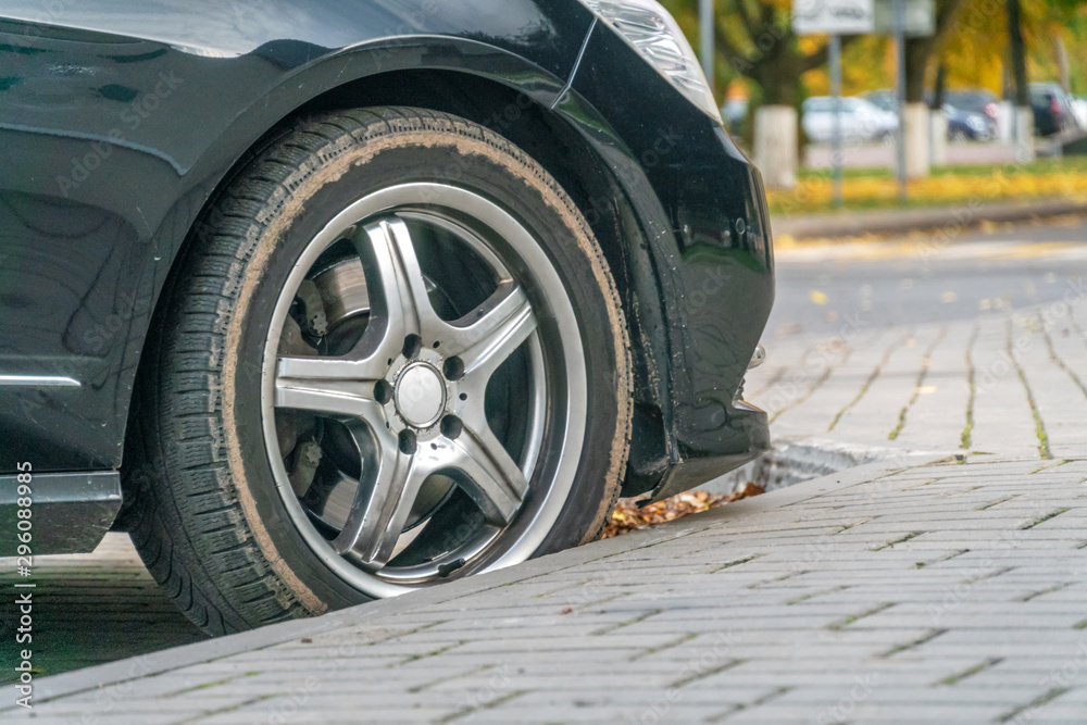 Side view of the wheel of a black car parked in autumn close up