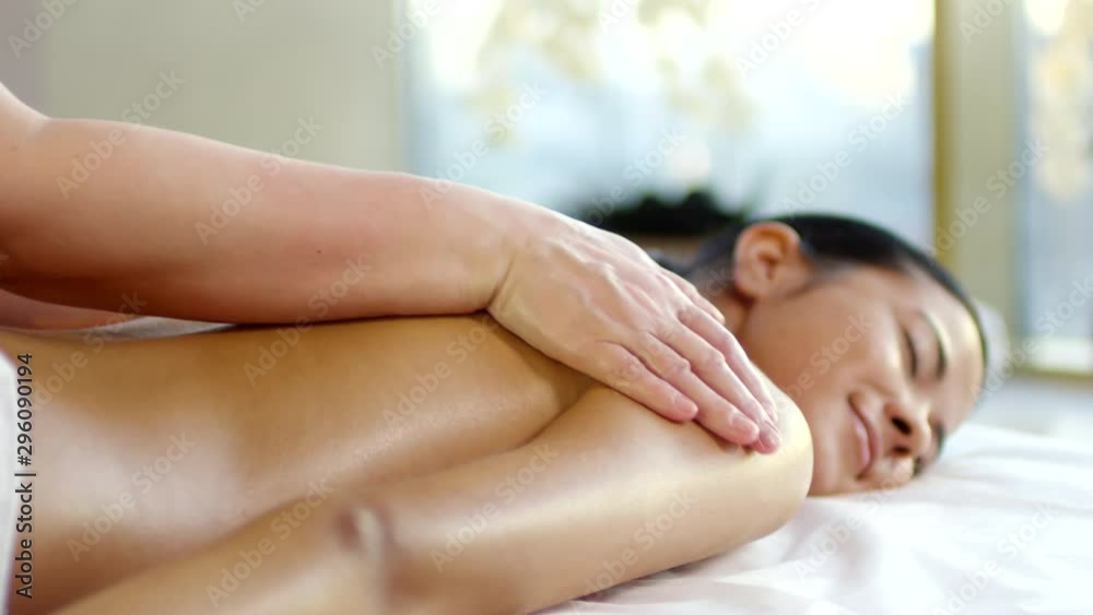 Tracking left of young mixed-race woman lying on massage table with closed eyes and receiving back massage Tracking left of young mixed-race woman lying on massage table with closed eyes and receiving back massage