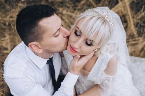 Stylish groom in a white shirt kisses a beautiful and smiling blonde bride. Wedding closeup portrait of lovers newlyweds. Photography and concept, emotions.