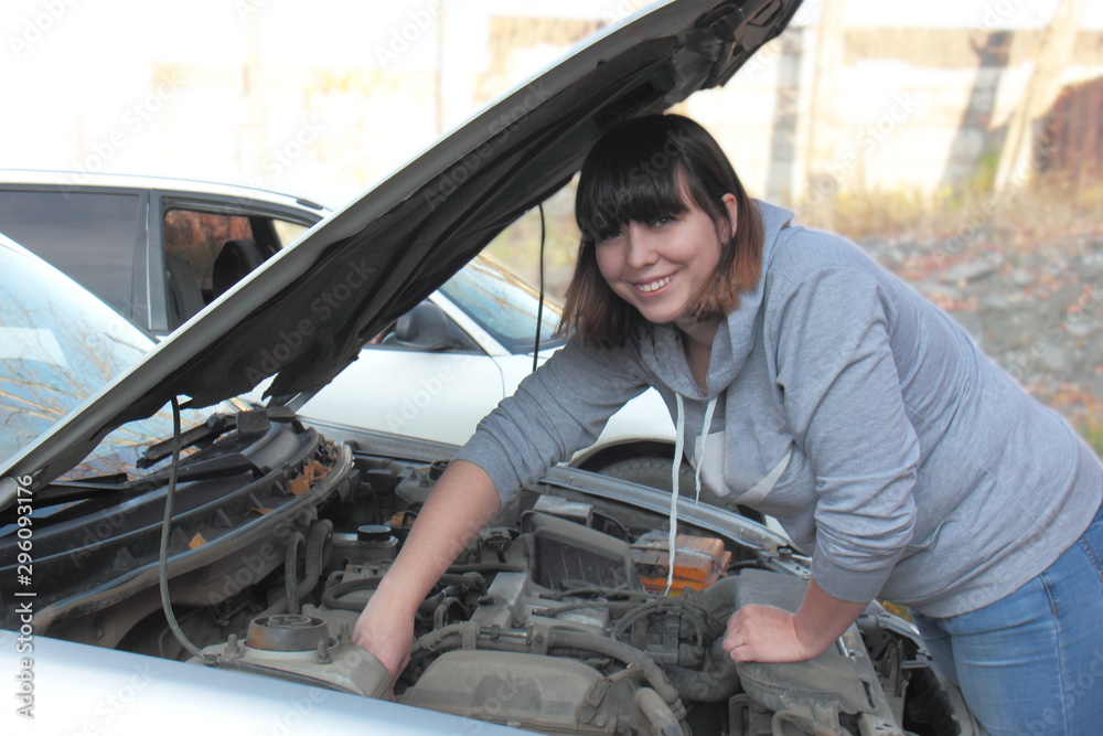 Beautiful young woman, brunette, repairs a car, looks under the hood Beautiful young woman, brunette, repairs a car, looks under the hood