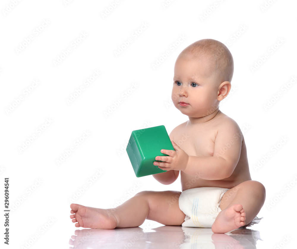 Quiet infant child baby boy in diaper is sitting on the floor with a green cube, playing, giving, taking on white Quiet infant child baby boy in diaper is sitting on the floor with a green cube, playing, giving, taking on white