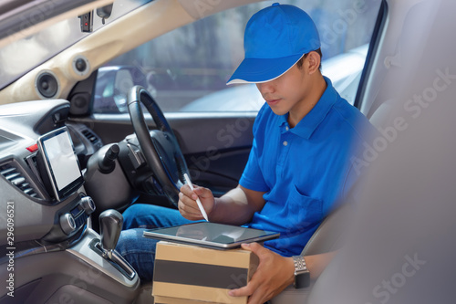 Happy young delivery man using tablet in van with carton box parcels on seat. Delivery service courier concept