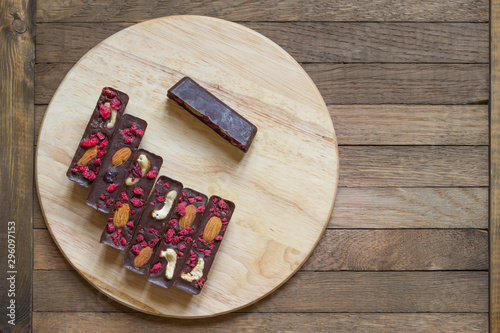 Vegan healthy homemade chocolate sticks with almonds, cashews and raspberries, lie on a round kitchen board on a wooden background. Top view. Copy space.