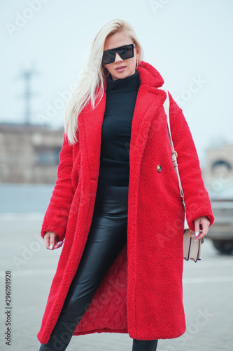 Fashion Week. Beautiful Girl dressed in a red faux fur coat and ugly boots walking street. Streetstyle fashion beauty trends ecology. Faux fur better than natural! Save animals! photo