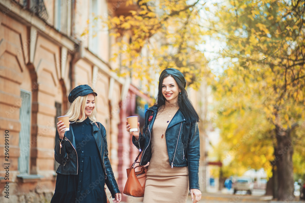 Autumn outdoor! Outdoors shot of young women with coffee on city street. Two fashion girls walking outdoor with cofee. Streetfashion friends lifestyle