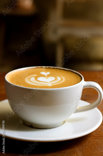 White cup of cappuccino with latte art on wooden background at coffee cafe.