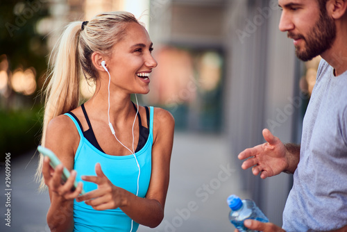 Modern woman and man jogging / exercising in urban surroundings and using cellphone at a pause / break.