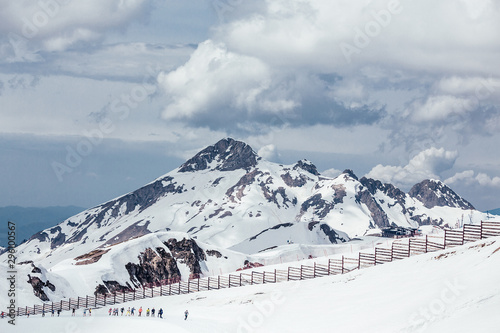 Beautiful snow-covered majestic mountain in a ski resort against a white lush cloud. The concept of rest in the ski resort and beautiful nature