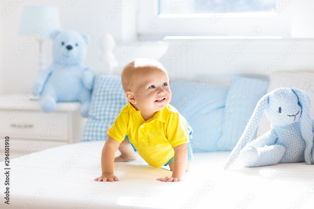 Baby boy playing on bed in sunny nursery Baby boy playing on bed in sunny nursery