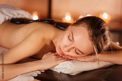 Beautiful young woman enjoying relaxing treatments the stone therapy at the spa salon by candlelight. The concept of relaxing and rejuvenating procedures