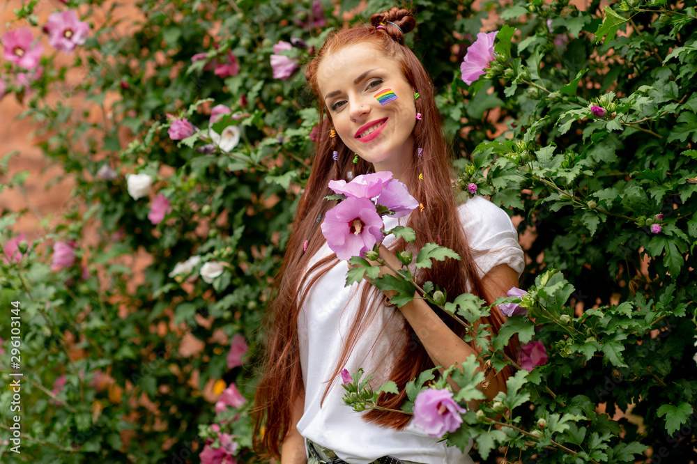 Cheerful lesbian with lgbt rainbow on her face posing in blooming flowers