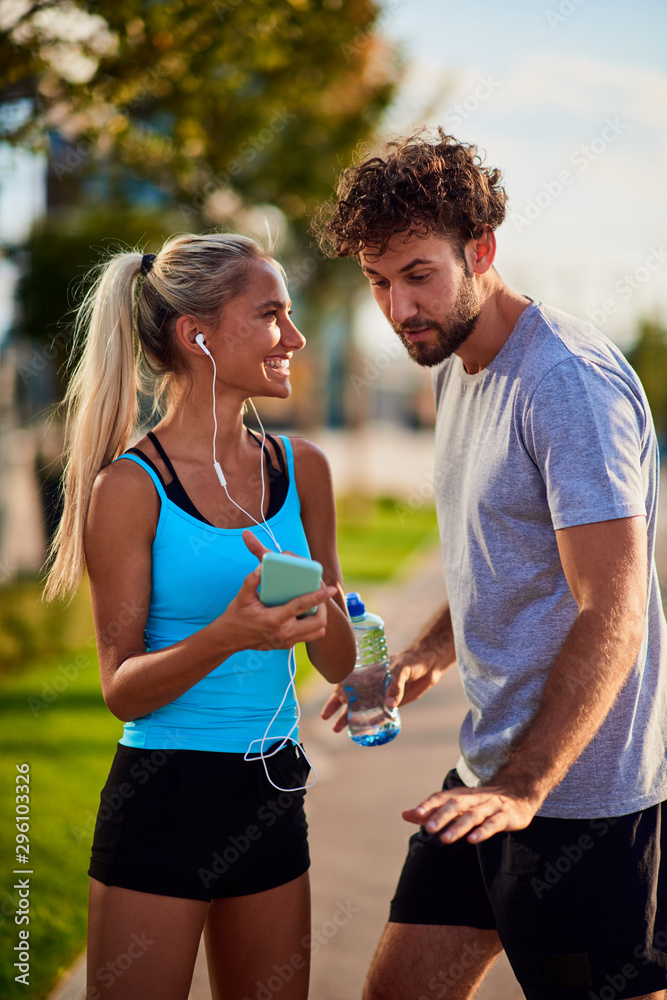 Modern woman and man jogging / exercising in urban surroundings and using cellphone at a pause / break. Modern woman and man jogging / exercising in urban surroundings and using cellphone at a pause / break.