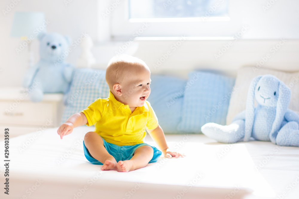 Baby boy playing on bed in sunny nursery Baby boy playing on bed in sunny nursery
