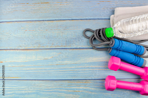 Top or flat lay view of dumbbells, towel, water and skipping rope with copy space area on blue wooden background. Healthy concept. Selective focus.